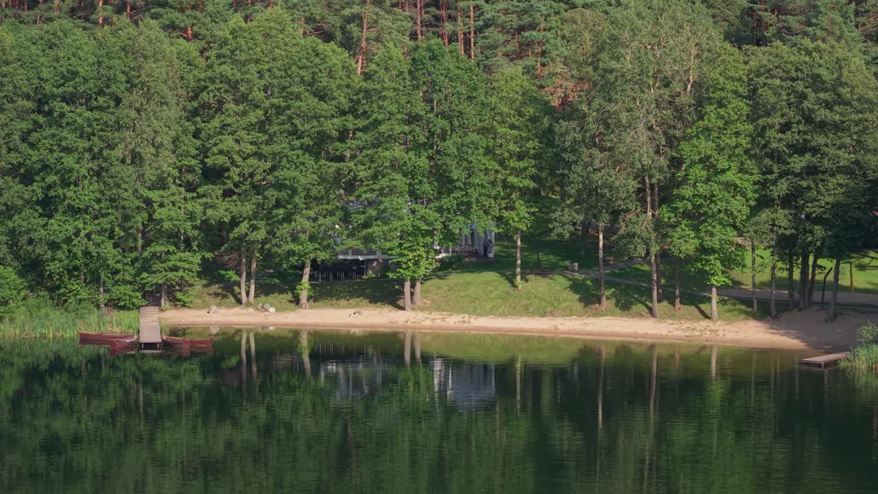 Scenic view of a tranquil forest lake with a sandy beach, small pier, and hidden event tent nestled among the trees