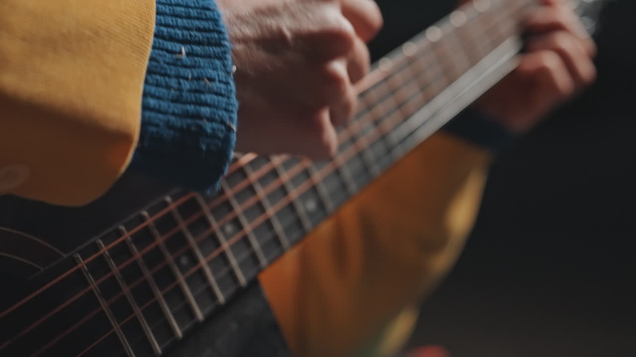 Closeup hands picking guitar strings in camping practice, focused technique shots of righthand fingerstyle and precise rhythm, camper rehearsing chord transitions with yellow jacket and blue cuff, low