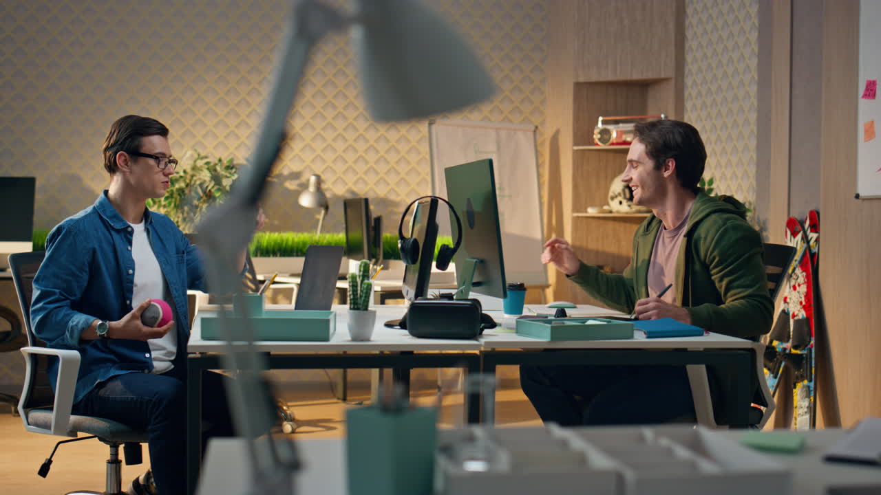 Afslappede mænd taler på kontoret. Ubekymrede designere arbejder roligt og drikker drikkevarer.