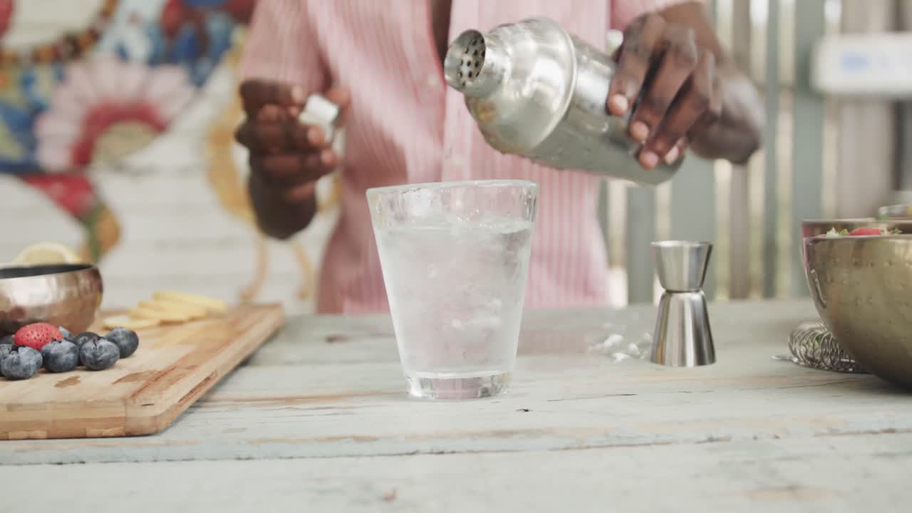 sección media del barman afroamericano vertiendo cóctel detrás del mostrador en el bar de la playa, cámara lenta