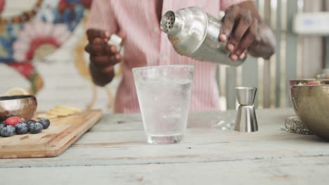 Midsection of african american barman pouring cocktail behind the counter at beach bar, slow motion