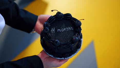 female hands holding a black sparkling cake with cherries. celebration of 11 months anniversary. top view close up.