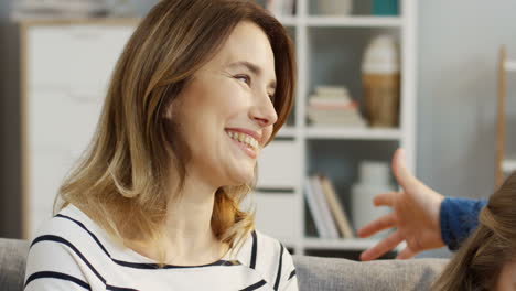 Close-Up-Of-The-Good-Looking-Happy-Family-Sitting-On-The-Couch-Close-To-Each-Other-While-Watching-Something-On-The-Smartphone-Or-The-Other-Device