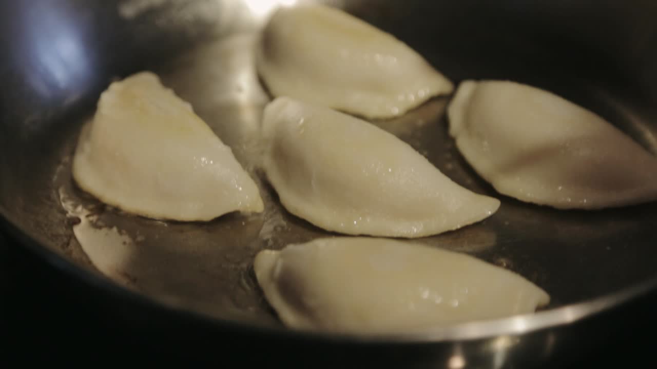 Canada - Frying Five Dumplings In A Stainless Pan With Cooking Oil Using Tongs - Closeup Shot
