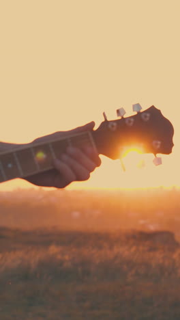 close young man hands playing guitar by tent in tourist camp at back setting sun light in warm autumn evening