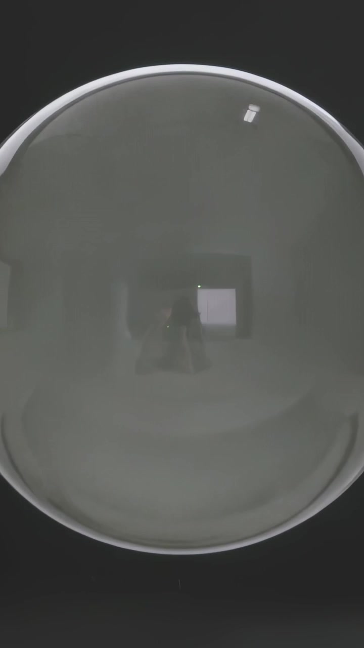 Video verticale: Sfera trasparente che reagisce, passando dal buio al bianco in una stanza, con strisce che rivelano un telefono.