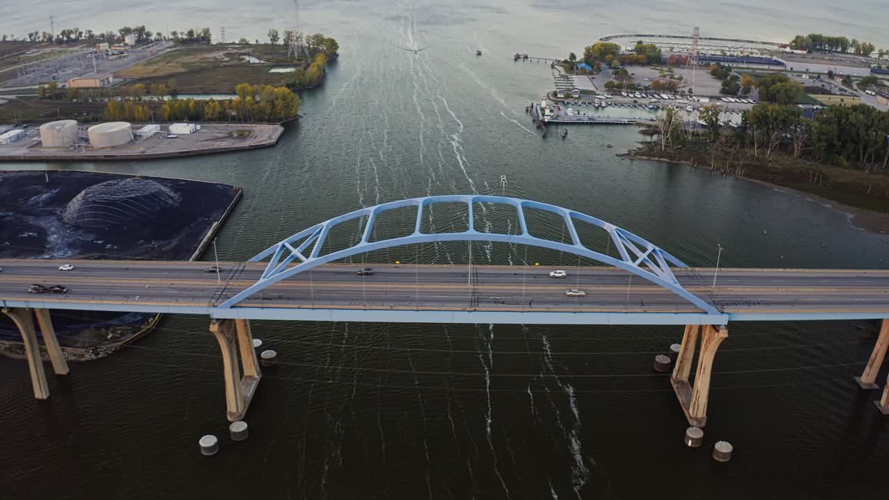 Cars move steadily across the Leo Frigo Memorial Bridge as it stretches over the calm waters of the Fox River, framed by industrial docks and soft evening light
