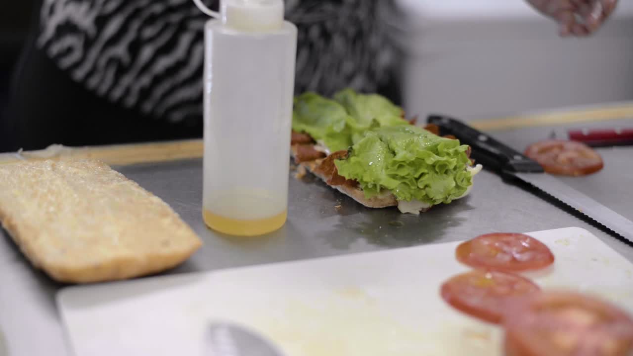 Woman chef cook preparing a salami ham pepperoni sandwich with lettuce olive oil and tomato on a baguette at a local cafe diner restaurant in Mexico Latin america. Healthy snack