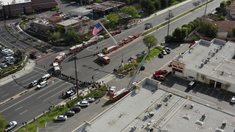 a group of firefights, police officers, fire trucks, police trucks wait for a funeral procession to honor a fallen officer