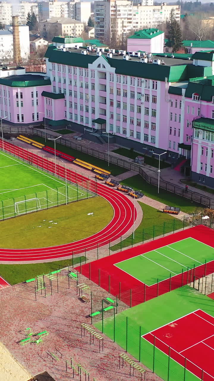 New fields for sports in the city. Sports complex with a modern stadium. Outdoor playgrounds on the urban background. Aerial view. Vertical video