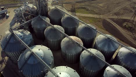 vol de drone au-dessus de barils métalliques ronds d'ascenseur par jour ensoleillé. vue du haut des structures rondes en béton armé pour le stockage du grain. complexe de construction de l'ascenceur de grain. séchage et récolte de stockage