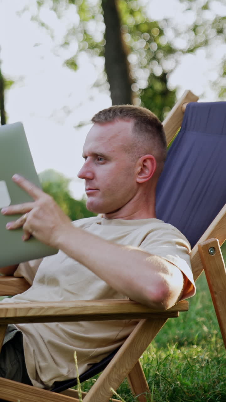 Caucasian man working remote in nature is feeling tired. Man takes a break covering his face with laptop. Vertical video