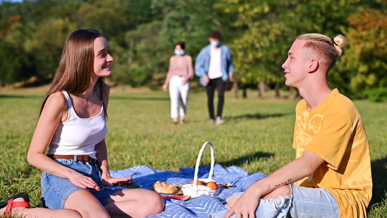 Group of friends gathering for a picnic in the park. Having fun while wearing protective medical masks. Corona Virus and pandemic idea