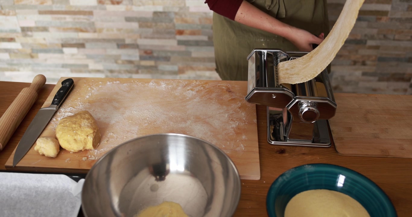 Person Using Manual Pasta Machine to Roll Fresh Dough