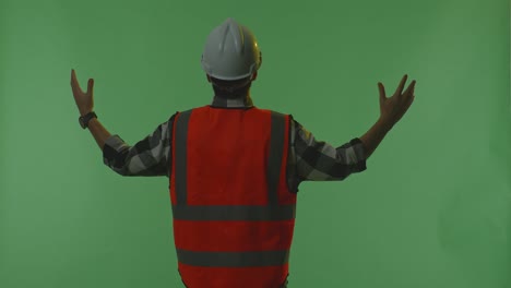 back view of a male engineer with safety helmet spreading arms while standing in the green screen background studio, during sunset or sunrise time