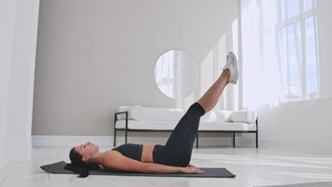 deportista entrenando en casa. atleta femenina en forma haciendo ejercicio de toque de dedo del pie con un solo brazo tendida en el suelo en un apartamento blanco.