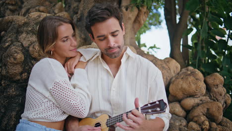 un macho romántico tocando la guitarra para una mujer en el bosque. una pareja de amor disfrutando.