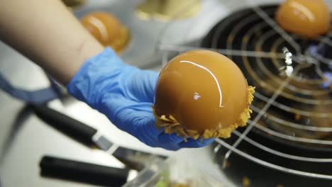 process of creating delicious dessserts. unrecognizable confectioners hands in blue gloves decorate caramel glazed cakes with layer of crisps on the bottom. close-up footage