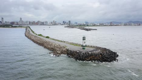 drone view flying over the path of the lighthouse with waves crashing into tetra concrete blocks of farol do molhe da barra de itajaí, santa catarina, brazil on a cloudy day