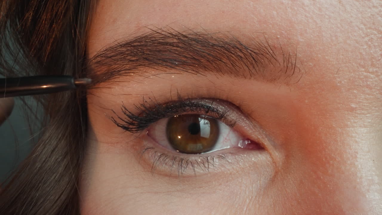 una mujer joven usa lápiz oscuro para resaltar el contorno de las cejas