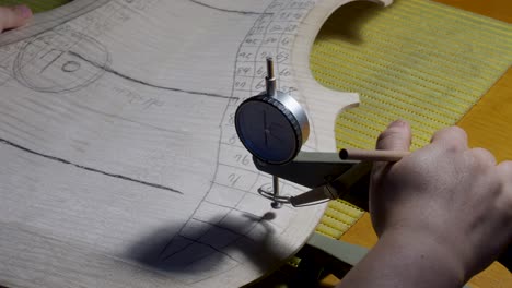 stringed instrument maker master luthier proceed with graduation work in cello back plate, use thickness gauge caliper, measure levels, use pencil write values on wood , cremona, italy workshop