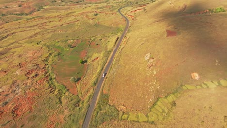 Vista-Aérea-De-Gran-Angular-De-Arriba-Hacia-Abajo-De-Una-Furgoneta-Conduciendo-Por-Una-Carretera-Asfaltada-En-El-Campo-De-Madagascar-En-Un-Día-Soleado