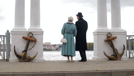 elderly couple standing by the water with decorative anchors