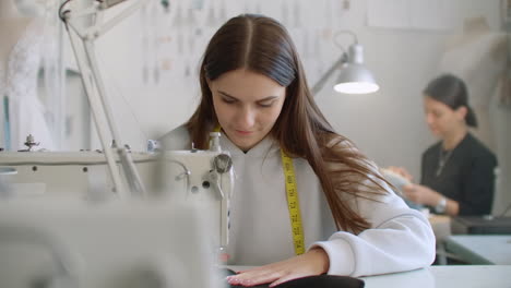 dolly shot of two female fashion designer working on the future clothes design while one of designer working with sketches on the background in the sew studio.