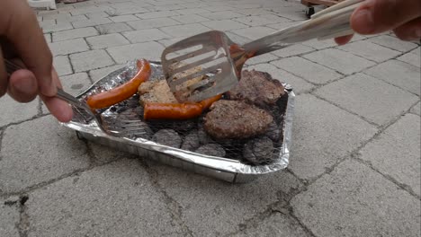 manos masculinas revisando salchichas, asando a la parrilla en mini barbacoa desechable