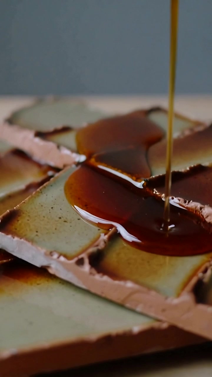 Video verticale: Flusso di sciroppo che scende e cola su quadrati di wafer impilati su un tagliere di legno.