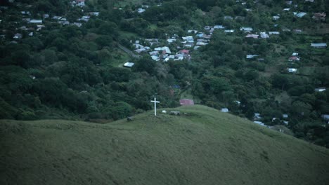 una cruz en la ladera de la montaña con un pueblo al fondo