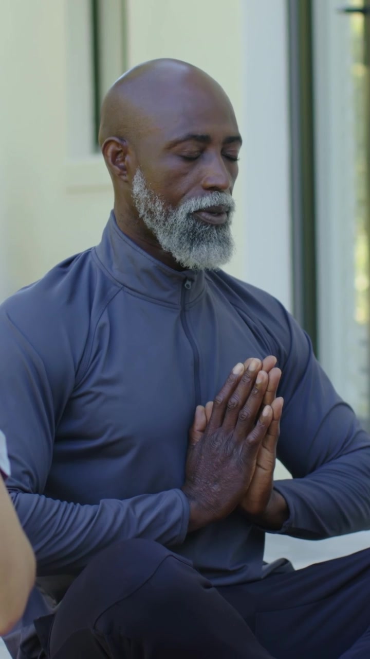Vertical video: Raising palms above head, mature man in grey holding prayer by glass doors for calm