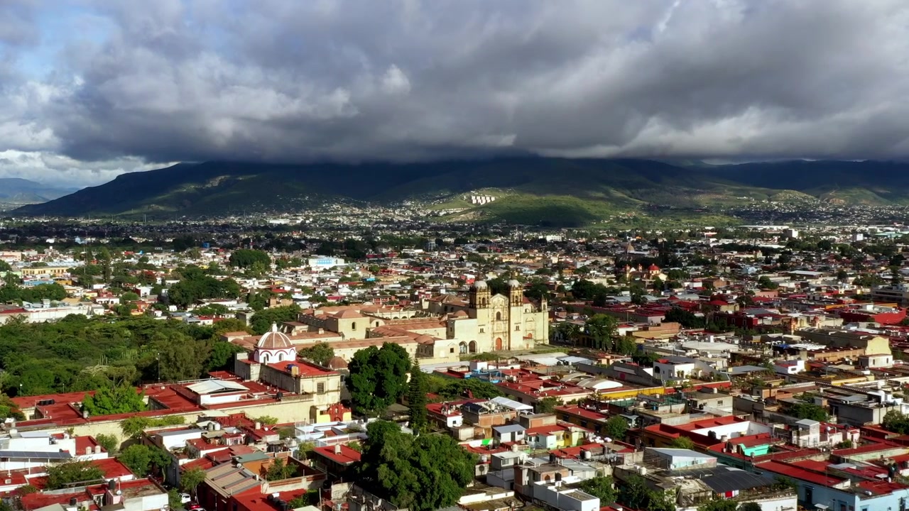 Vista aérea de cidade histórica com catedral, edifícios densos e nuvens de tempestade dramáticas acima da serra, em um cenário urbano pitoresco.