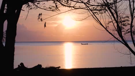 Local-fishing-boat-traveling-a-peaceful,-calm-and-placid-ocean-during-beautiful-heavenly-sunrise-with-pink-sky-on-tropical-island-in-Timor-Leste,-Southeast-Asia