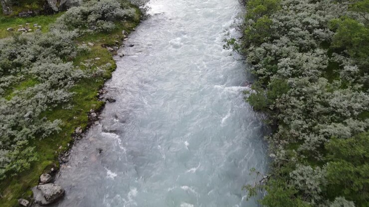 drone flying over stream in Norwegain mountains, tilting up and revealing a valley and winding road
