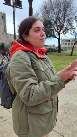 a woman wearing a green jacket and a red hoodie is holding a cell phone