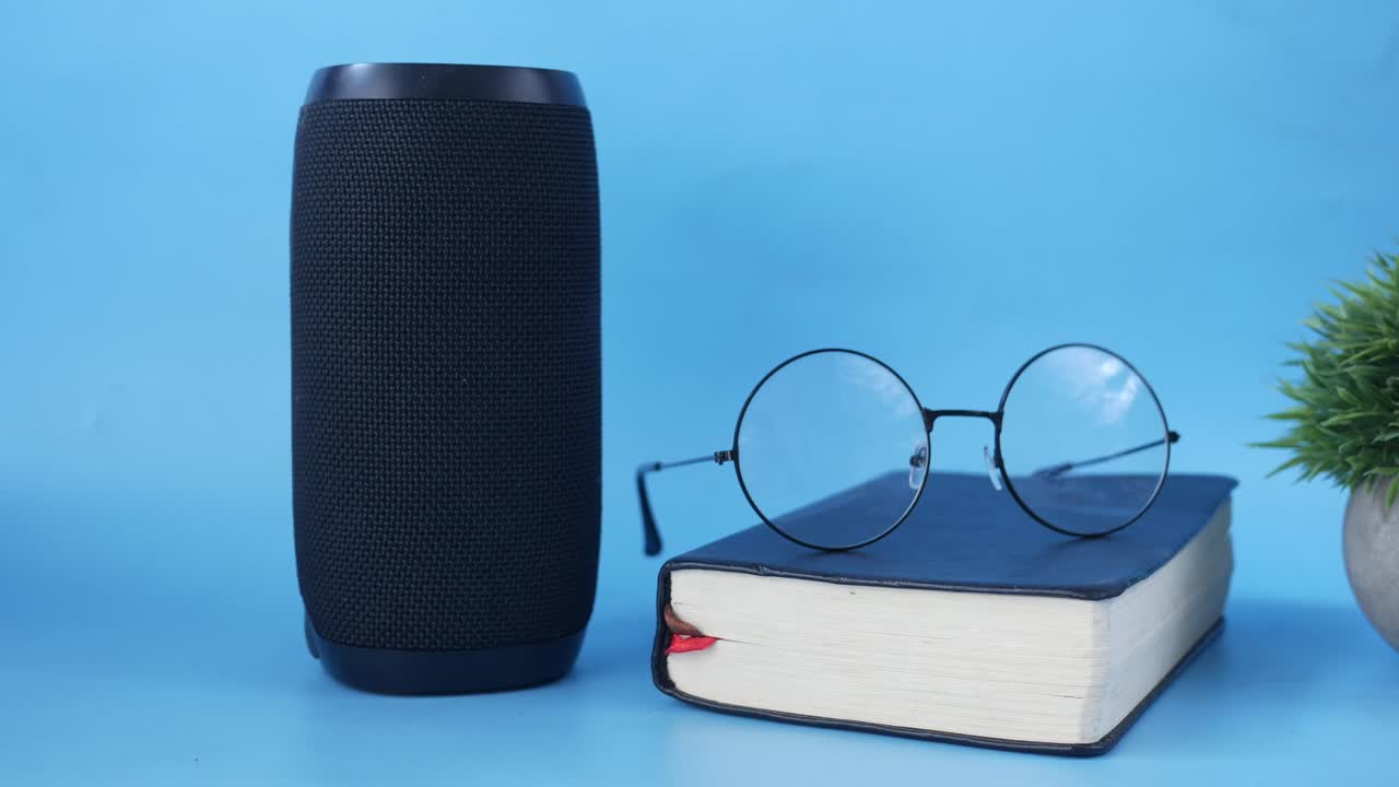 altavoz portátil, libro y gafas sobre un fondo azul