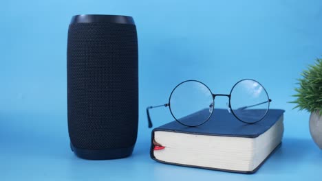 portable speaker, book, and glasses on a blue background