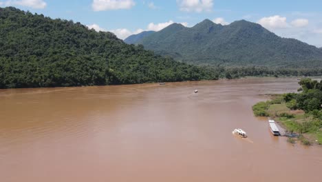 Aerial-Flying-Over-Mekong-River-Bend-On-Sunny-Day-With-River-Boat-Seen-Crossing-It-In-Luang-Prabang