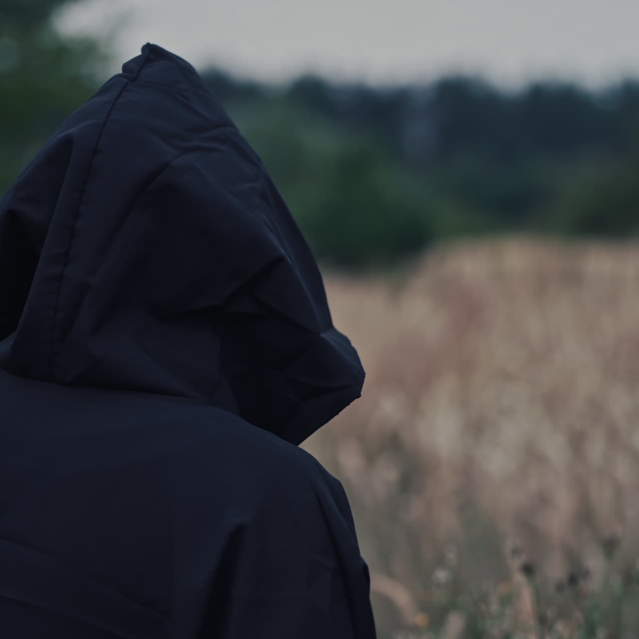 Close-up scary face of ghost. Nightmare in black costume with hood looking at camera and going away on the field. Fright concept. Halloween.