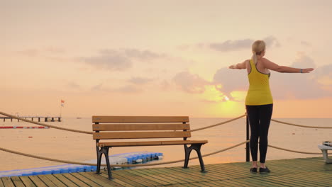 active woman doing exercises on the pier by the sea where the current that the sun rose start a new