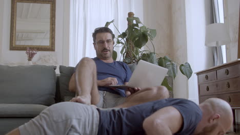 gay sentado en el sofá, animando a su compañero que hace flexiones