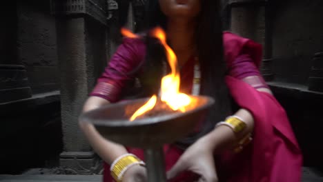 beautiful-Indian-girl-in-old-stepwell-wearing-traditional-Indian-red-saree,-gold-jewellery-and-bangles-holding-fire-plate