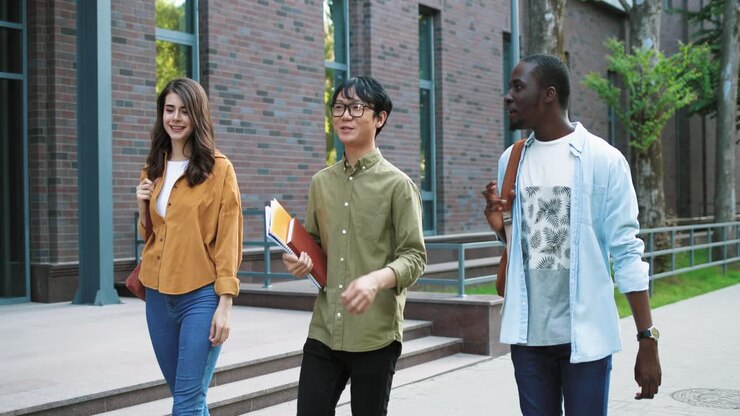 Caucasian, asian and african american students talking and laughing while walking down the street near the college