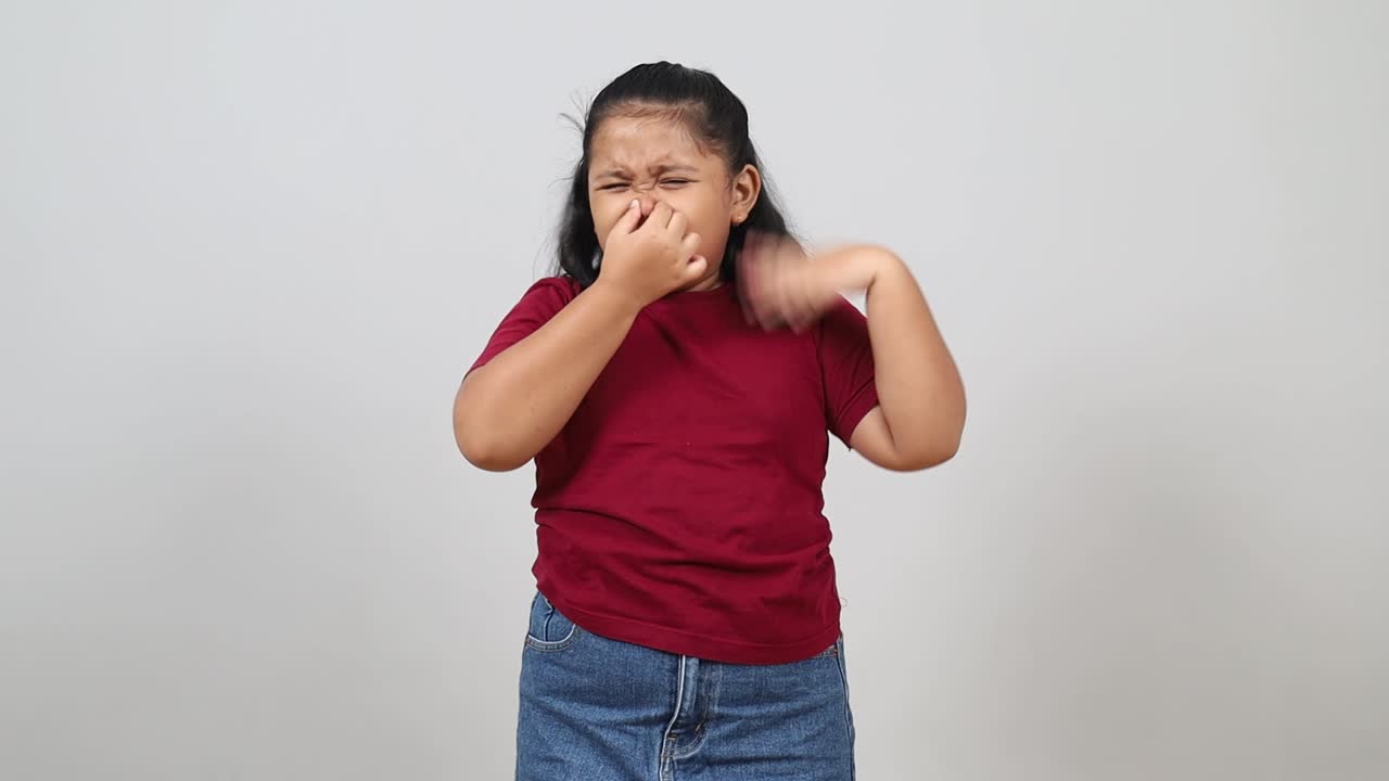 Bambina asiatica che si annusa l'ascella, si tappa il naso con la mano, mostrando disgusto per il forte odore corporeo. Odore corporeo sgradevole, reazione di fastidio all'odore.