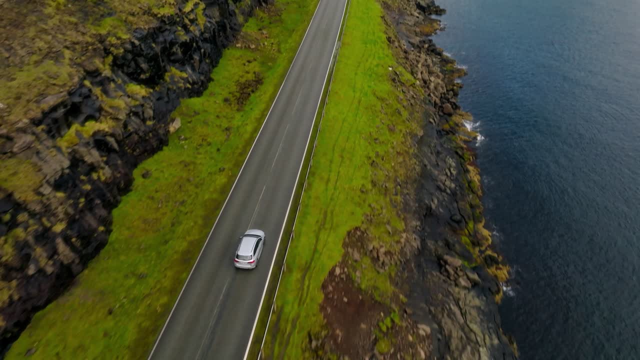 A lone car drives along a scenic coastal road in the Faroe Islands, showing isolation