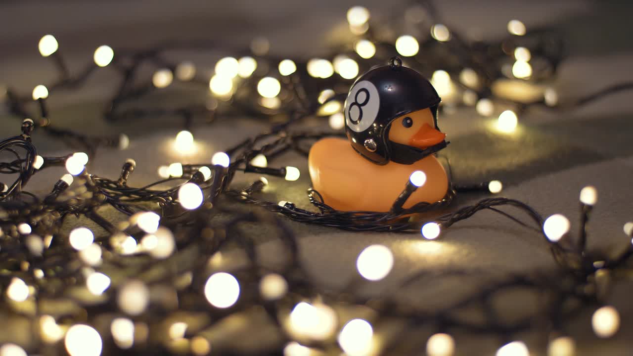 fotografía en primer plano de un pato de goma con un casco de motocicleta hecho a mano sobre el fondo de una guirnalda de navidad