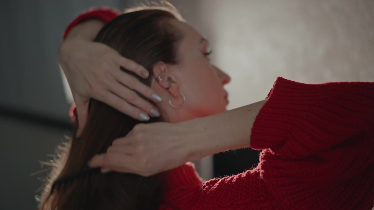Vista ravvicinata di tre quarti posteriore di una donna che liscia i lunghi capelli castani con le mani e un pettine, mostrando un movimento naturale di cura mentre le ciocche si raccolgono, si sollevano e cadono sotto una morbida retroilluminazione da studio con una delicata atmosfera da salone