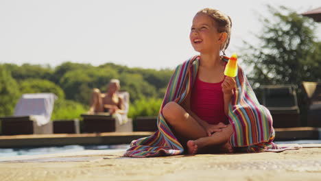 Familia-En-Vacaciones-De-Verano-Con-Una-Chica-Comiendo-Polo-De-Hielo-Al-Borde-De-La-Piscina