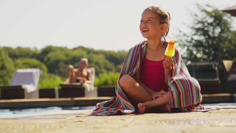 familia en vacaciones de verano con una chica comiendo caramelo de hielo en el borde de la piscina